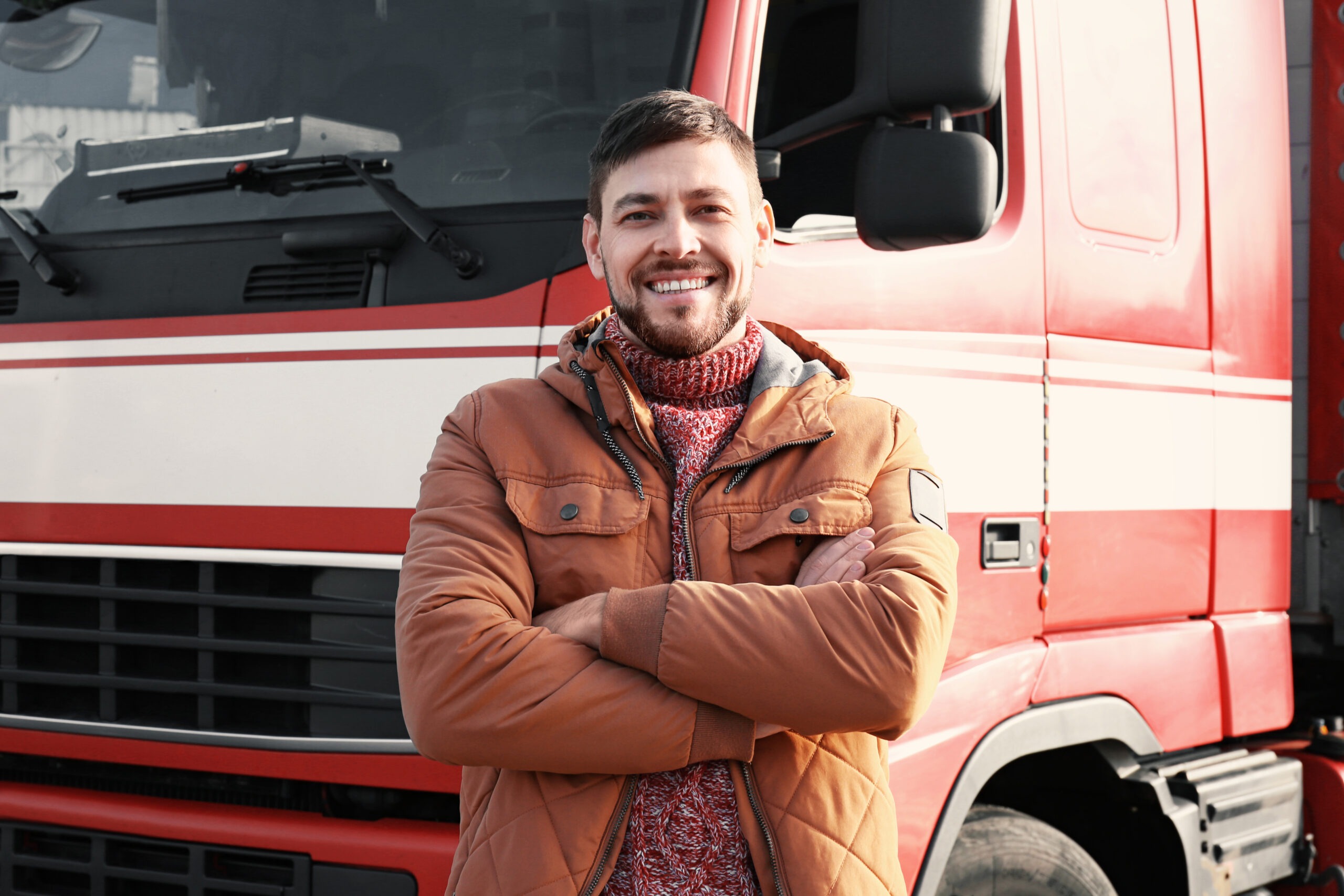 Smiling man in a brown jacket stands in front of a red fire truck
