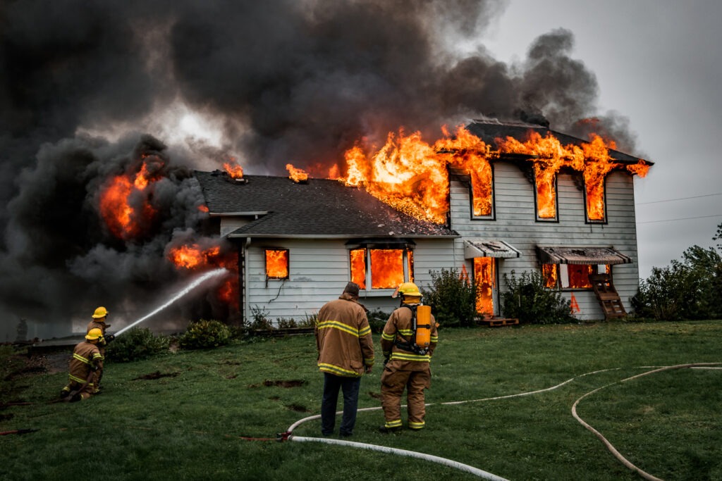 Fire engulfs a two-story house, with firefighters using hoses to battle the flames